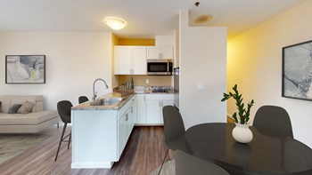 L-shaped kitchen with white cabinets and hard wood style flooring. Sink is on peninsula that looks into living room. - Photo Gallery 3