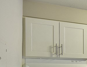 Kitchen with white cabinets and grey countertops. Image contains a white oven, sink and white dishwasher. One window and wood style flooring. - Photo Gallery 6