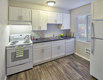 Kitchen with white cabinets and grey countertops. Image contains a white oven, sink and white dishwasher. One window and wood style flooring.at Woodhaven, Everett, Washington