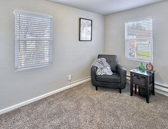 Carpeted living space, with two windows on two walls. Staged with a chair and side table.at Woodhaven, Everett, WA 98203 - Photo Gallery 4