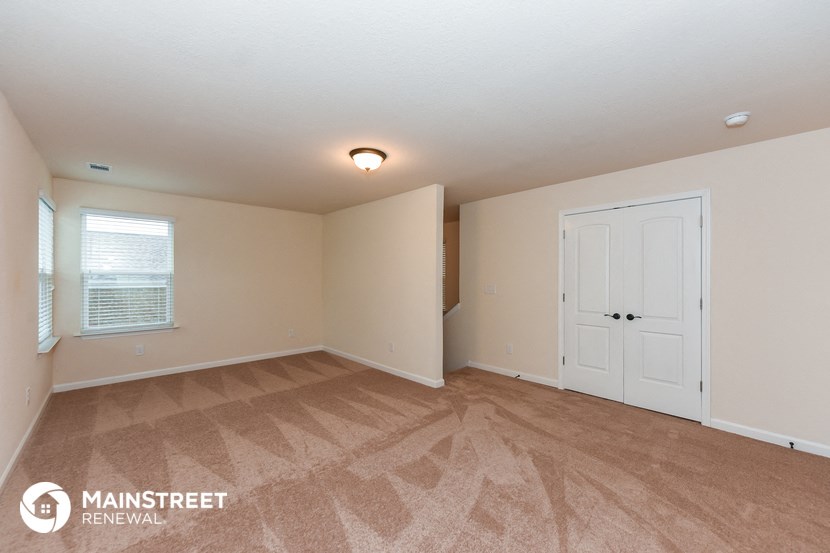 the living room of a house with a white door and carpeted flooring