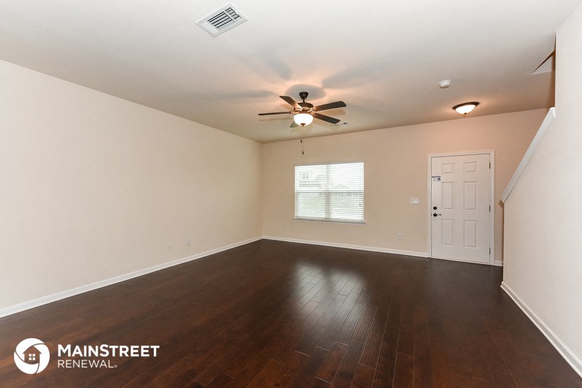 the spacious living room with hardwood flooring and a ceiling fan