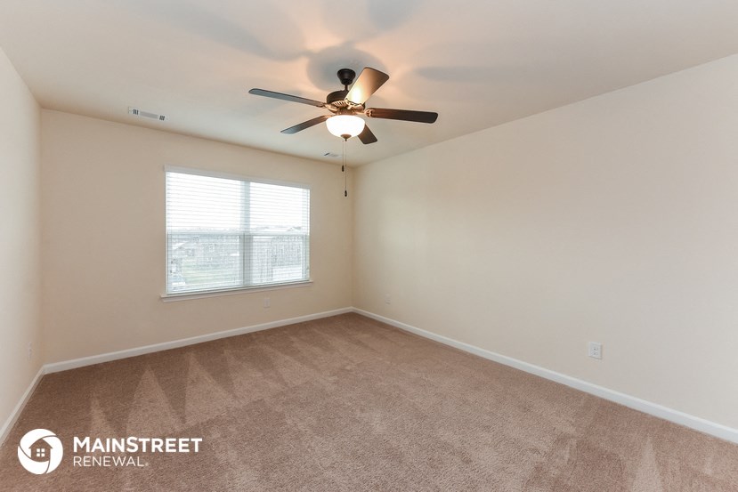 the living room of an apartment with carpet and a ceiling fan