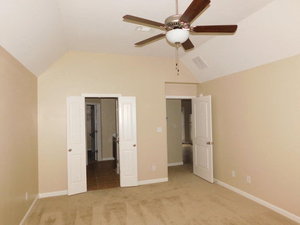 an empty living room with a ceiling fan and a door to a hallway