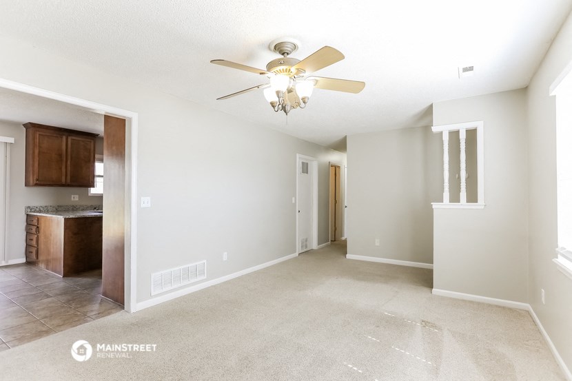 an empty living room with a ceiling fan and a kitchen