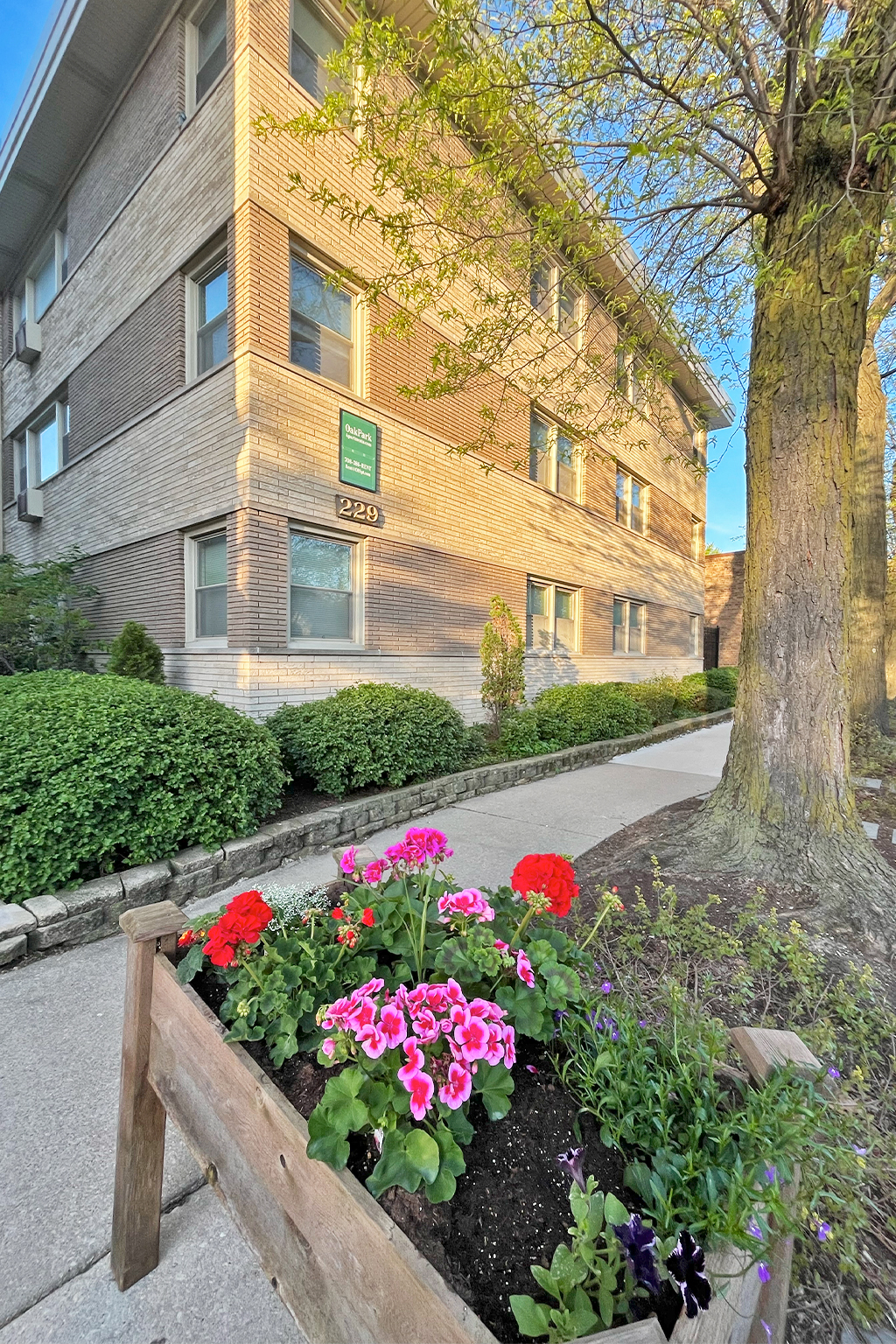A building with a green sign on the front and a flower bed in front of it.