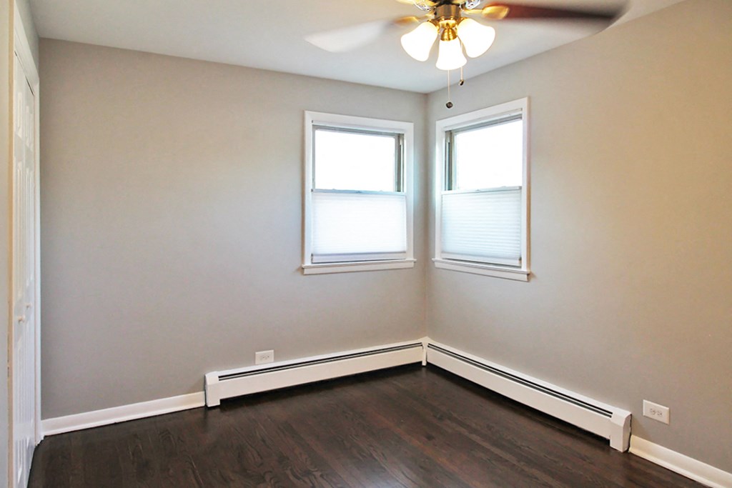 an empty room with wood flooring and two windows and a ceiling fan