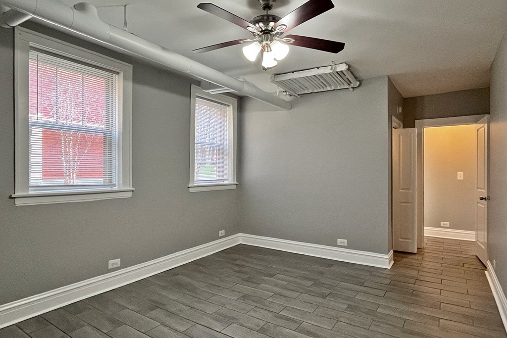 A room with a ceiling fan and two windows.