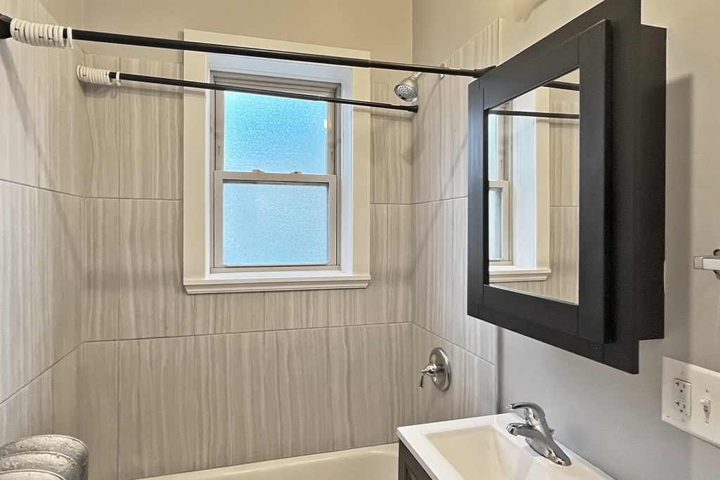 A bathroom with a tub, sink, mirror, and a window.
