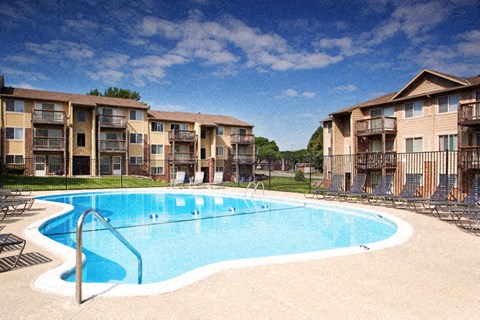 a large swimming pool with tanning deck chairs and apartment buildings in the background