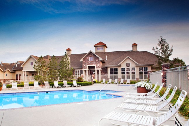 a swimming pool with white chairs in front of a large house