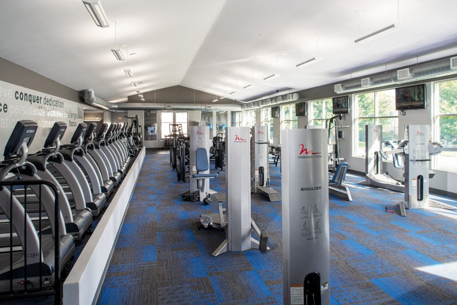 a gym with rows of cardio machines and chairs and windows