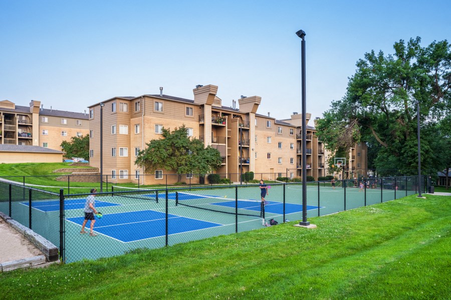 two people playing tennis on a tennis court in front of an apartment building