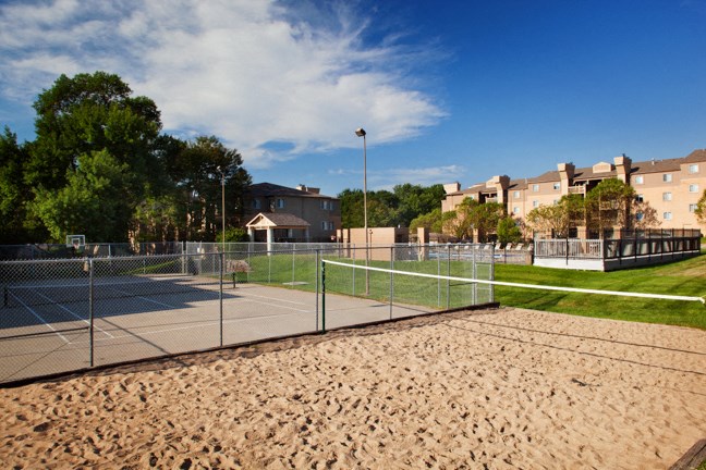 a tennis court with sand in the foreground and buildings in the background