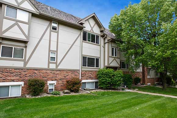 an apartment building with a green lawn and trees