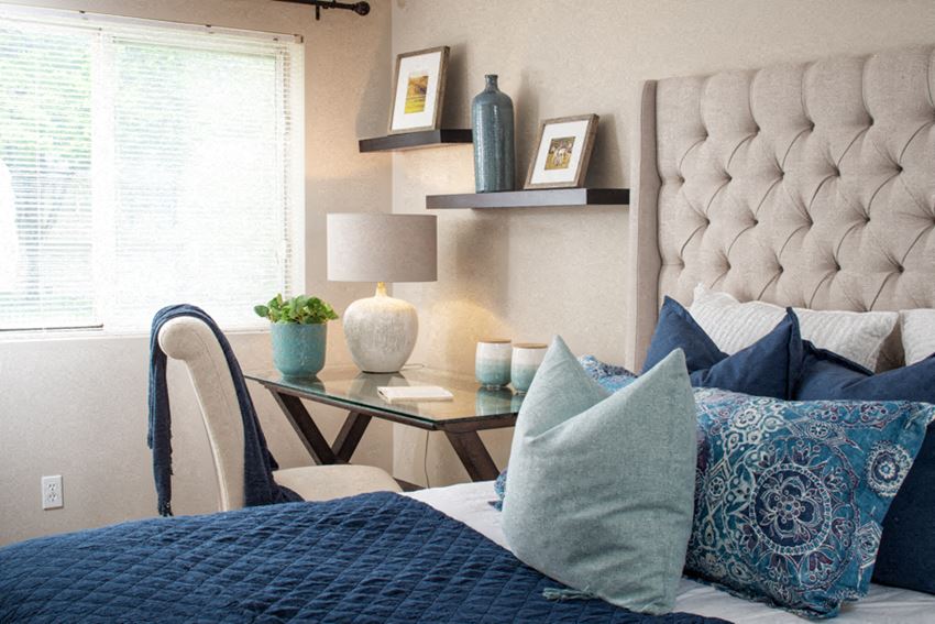 a bedroom with a bed with blue and white pillows and a desk with a lamp and
