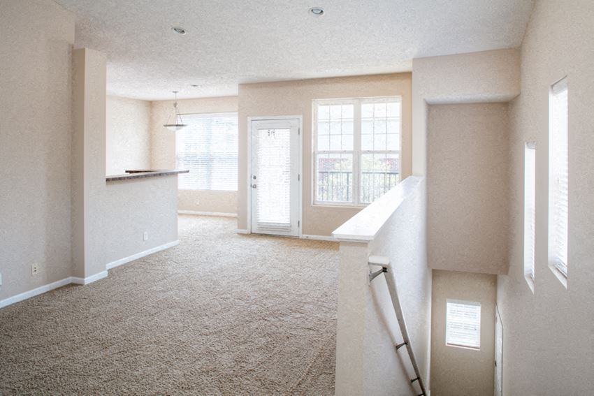 an empty living room with a kitchen in the background