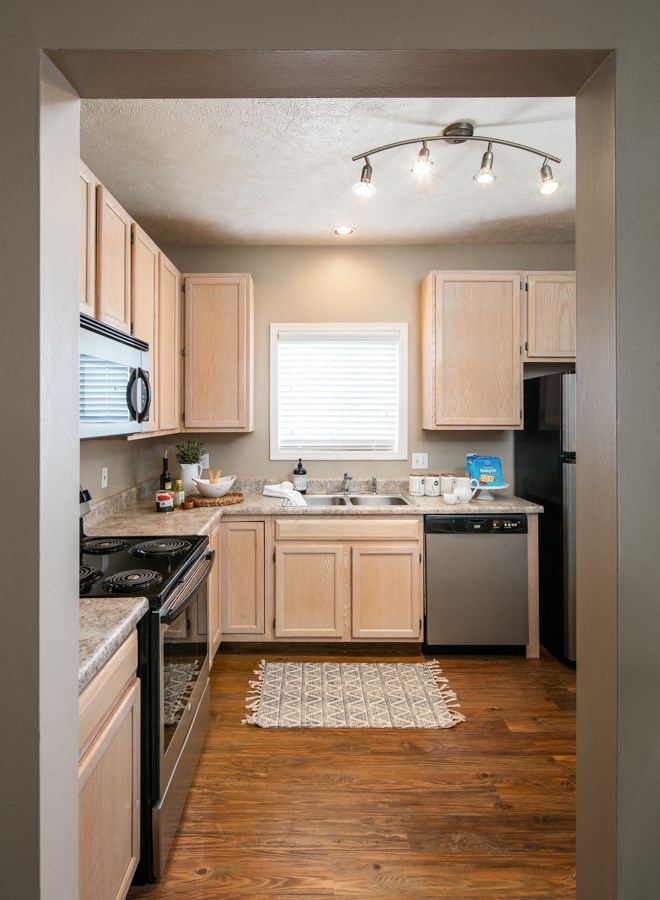 a kitchen with wooden cabinets and black appliances and a white rug