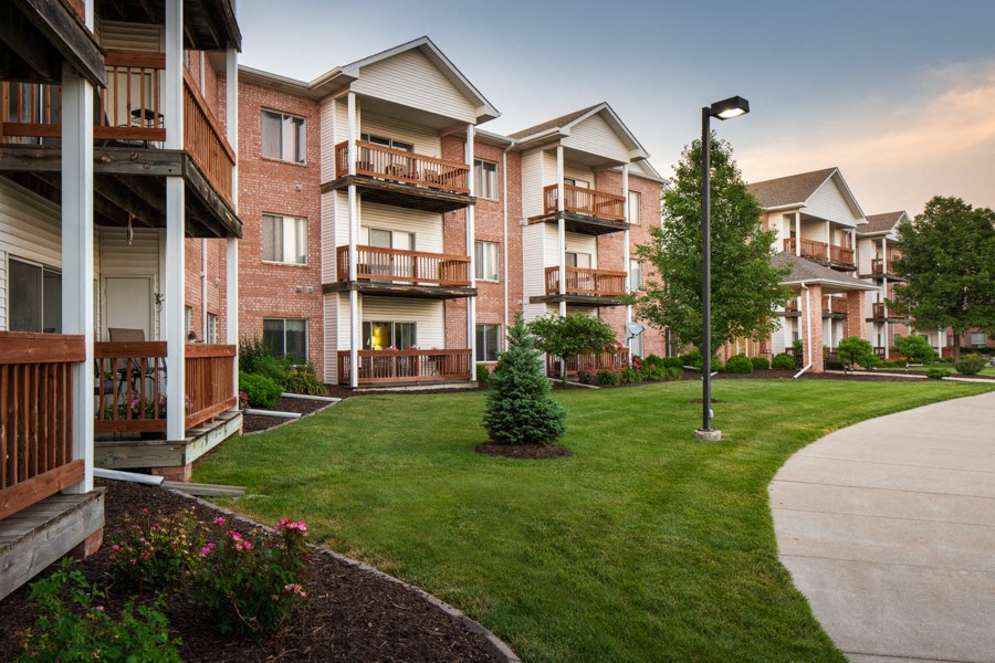 an exterior view of an apartment complex with green grass and a sidewalk