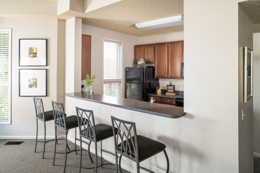 a kitchen with a bar with three chairs and a refrigerator