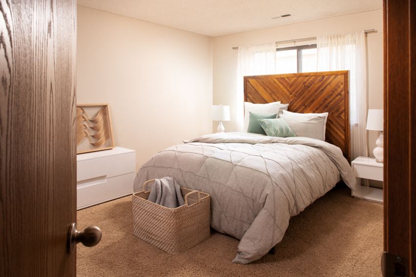 a bedroom with a bed with a wooden headboard and a basket at the foot of the