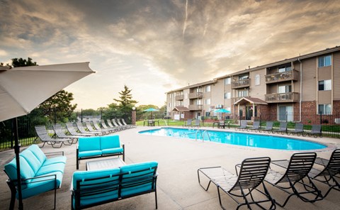 a swimming pool with blue chairs and umbrellas in front of an apartment building