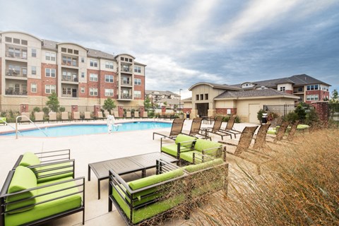 a swimming pool with green chairs and chairs next to an apartment building