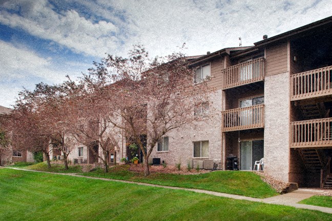a brick apartment building with a lawn and flowering trees