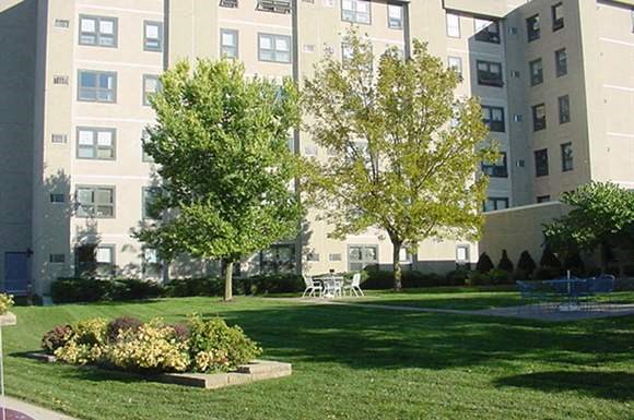 a park with trees and flowers in front of an apartment building