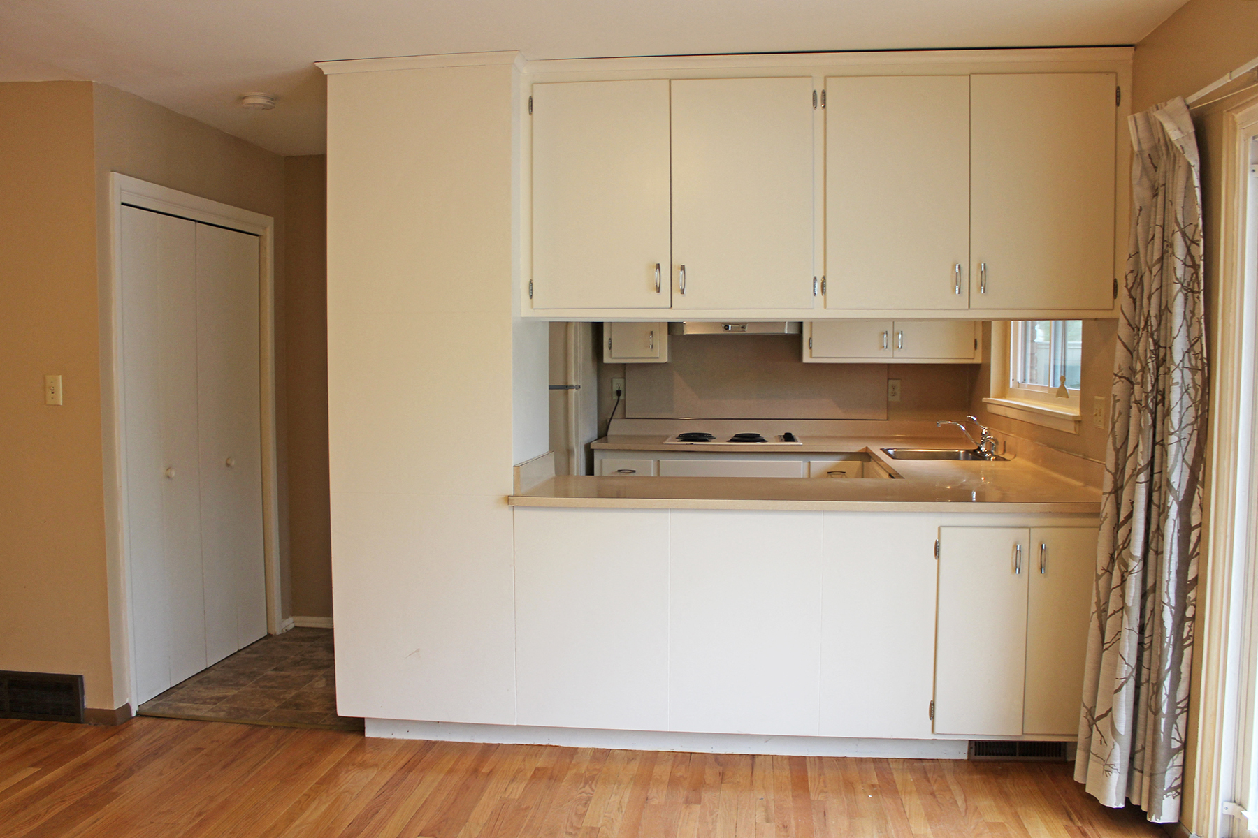 an empty kitchen with white cabinets and a window