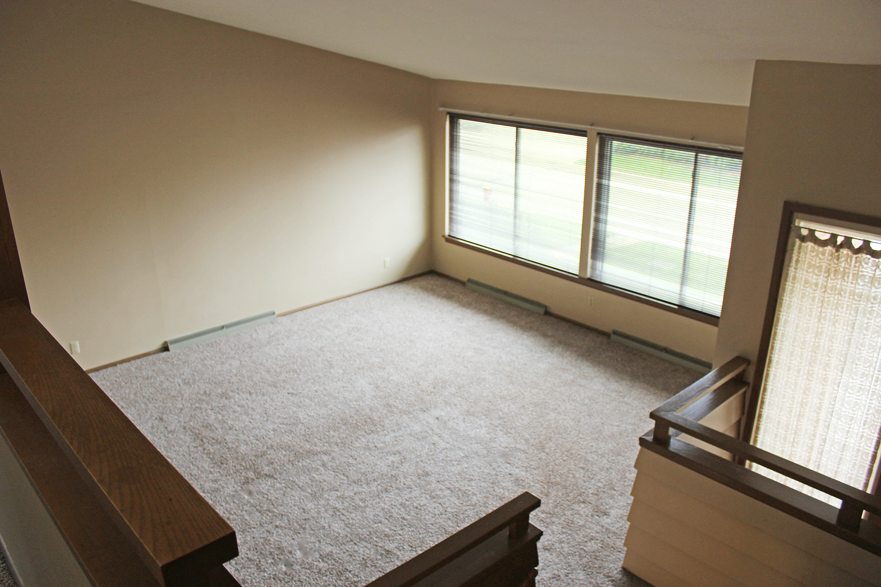 an empty living room with a carpeted floor and three windows
