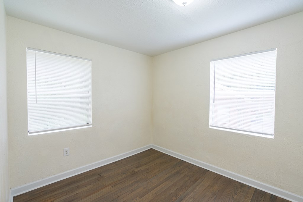 an empty room with wood flooring and two windows