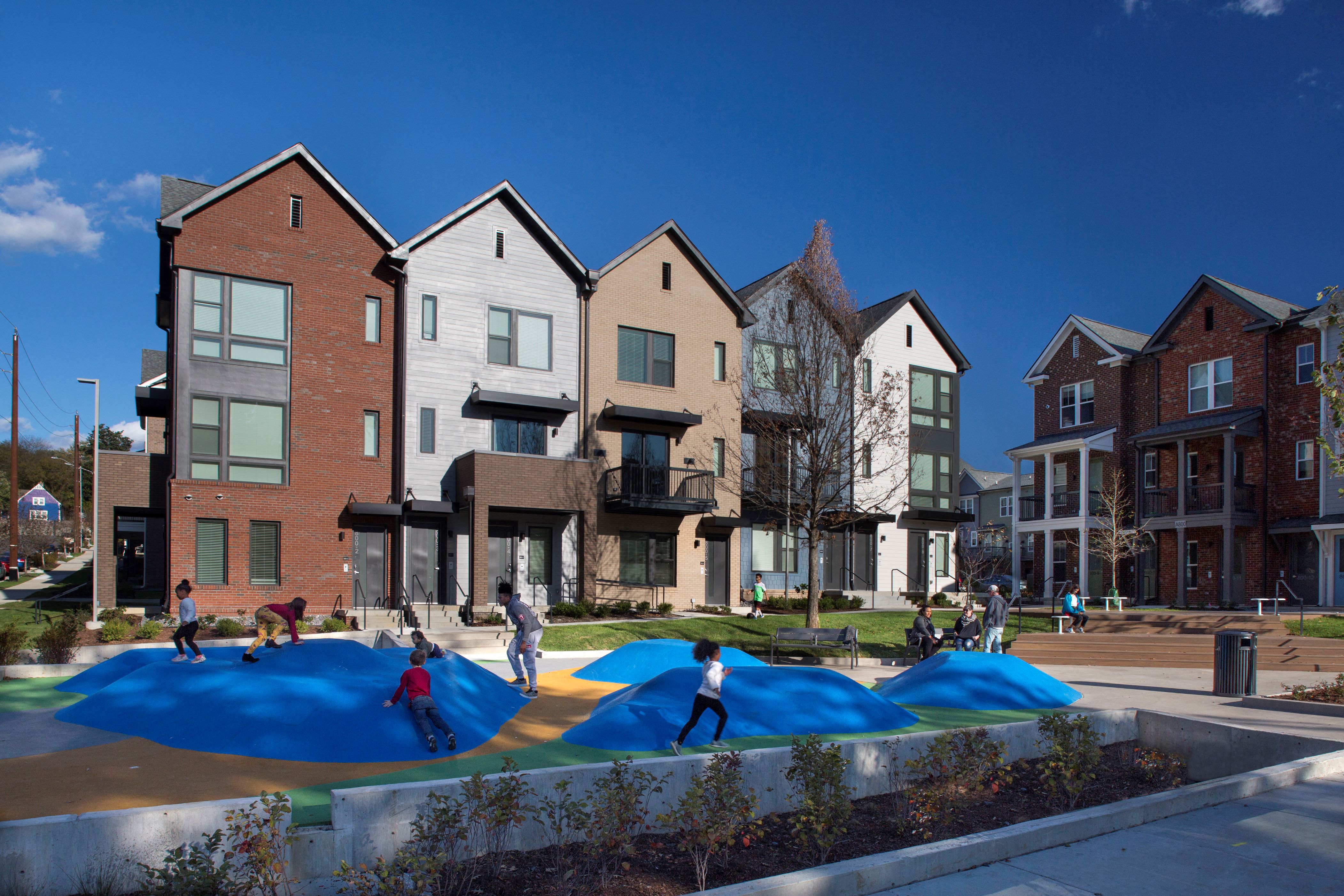 A playground with a blue surface is surrounded by a row of houses.