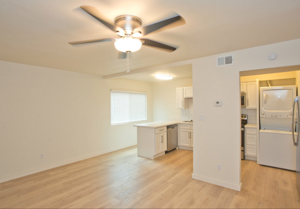 an empty living room with a ceiling fan and a kitchen