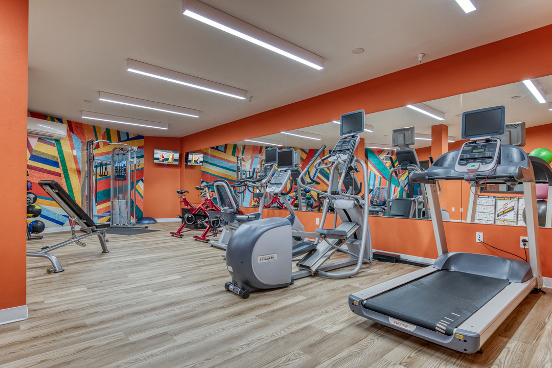 a gym with cardio machines and exercise equipment in a building with orange walls