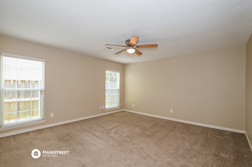 an empty living room with a ceiling fan and two windows