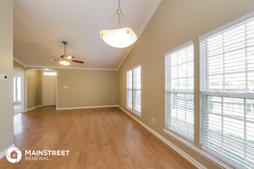 an empty living room with large windows and a ceiling fan