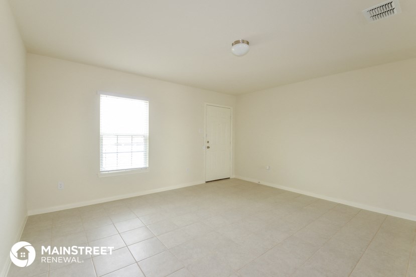 an empty living room with white tile and a window