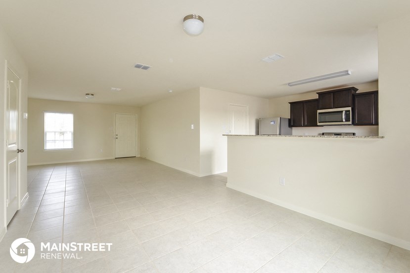 an empty kitchen and living room with white tile flooring and a counter