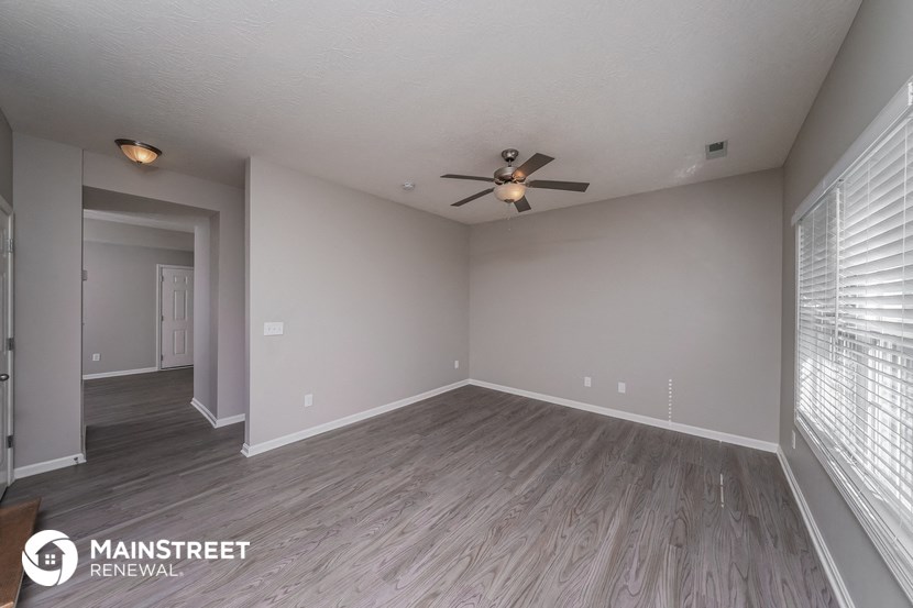 the spacious living room with wood flooring and a ceiling fan