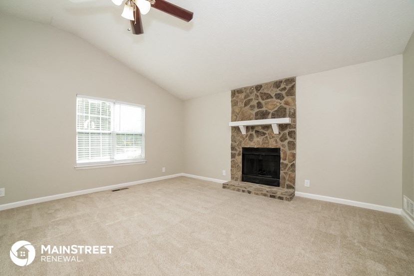 the living room has a stone fireplace and carpeted flooring