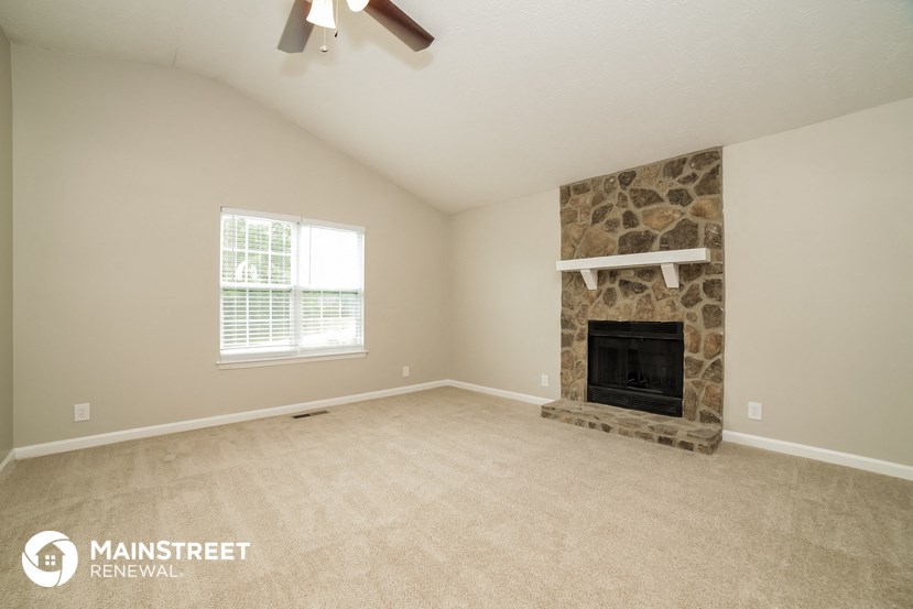 the living room has a stone fireplace and carpeted flooring