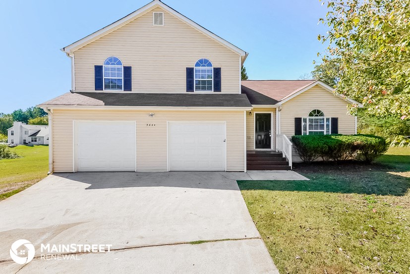 a yellow house with a white garage door and a driveway
