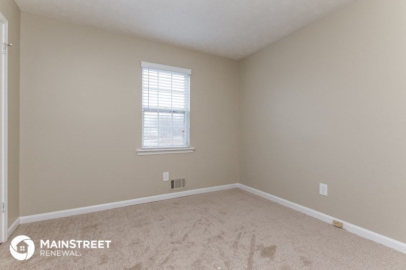 the bedroom of a home with beige carpet and a window