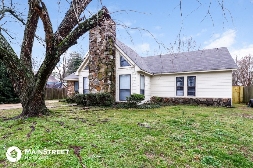 a white house with a stone chimney and a tree in the yard