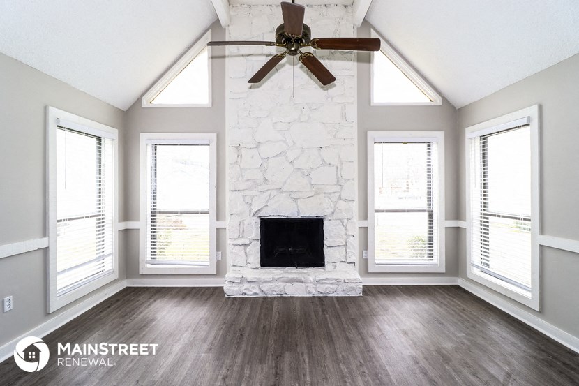 a living room with a stone fireplace and a ceiling fan