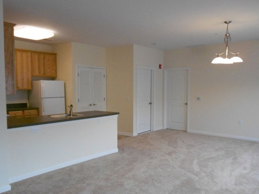 an empty living room with a kitchen and a refrigerator
