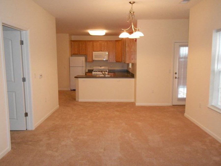 an empty living room and kitchen with a refrigerator and a sink