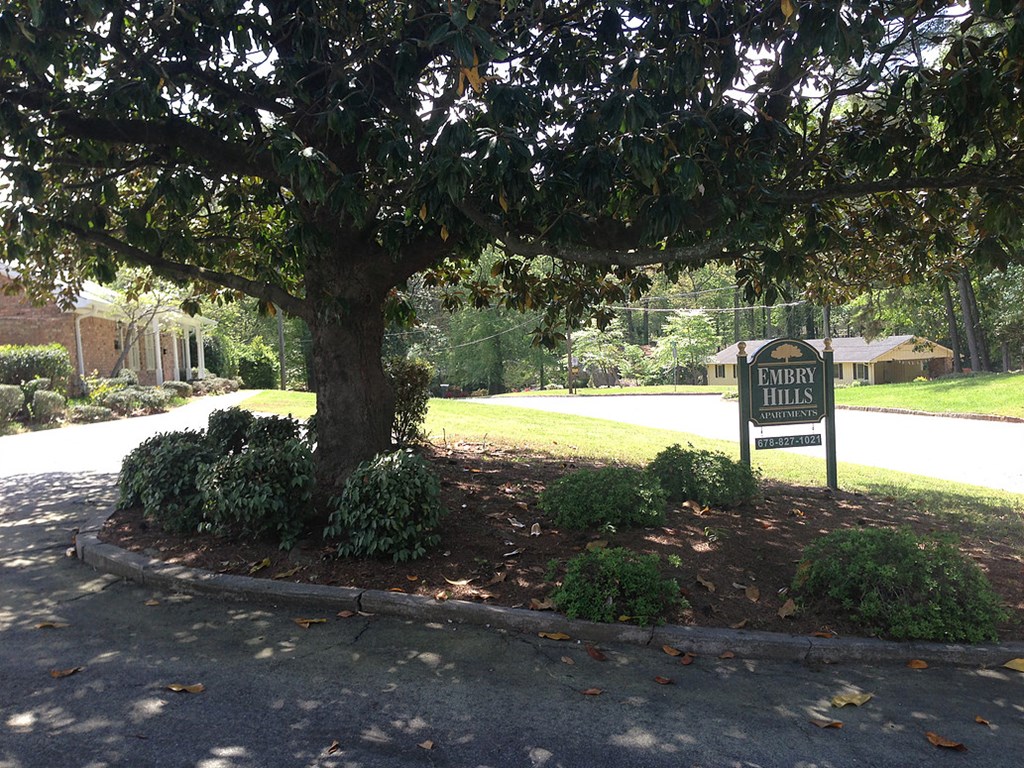a sign sitting under a tree in front of a driveway