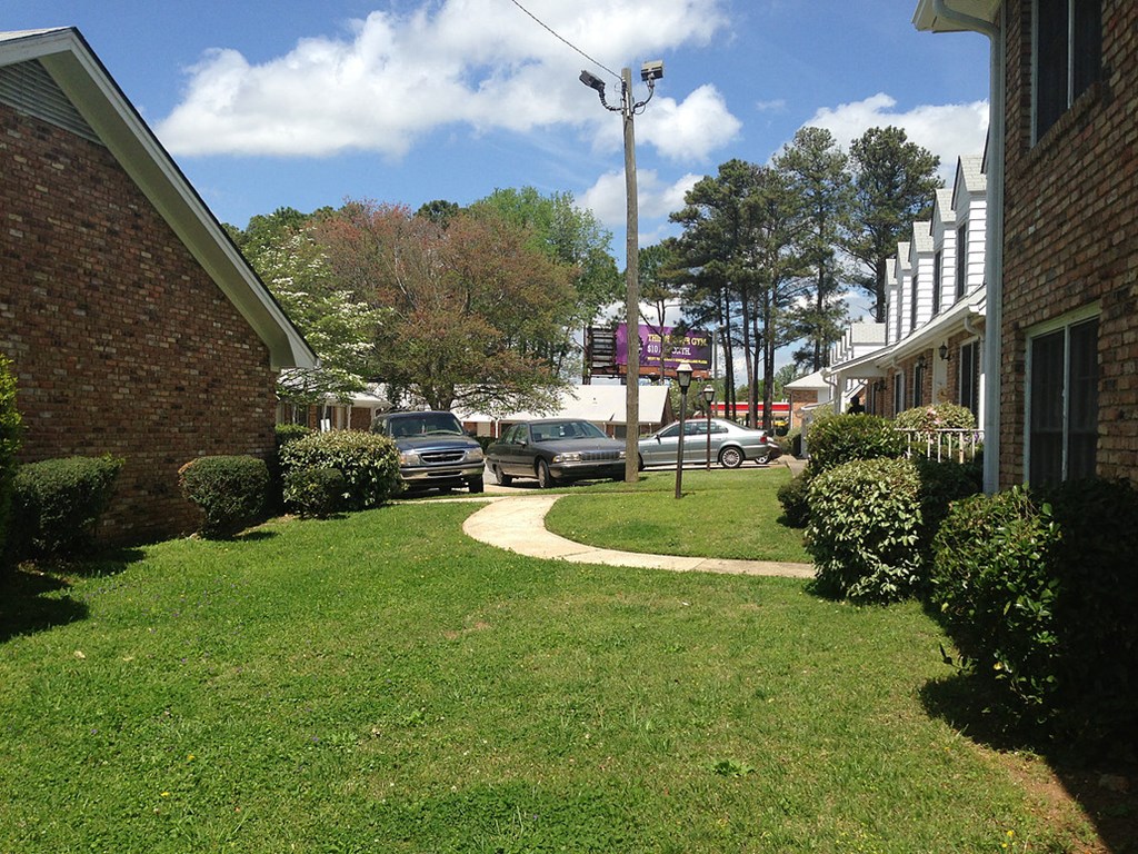 a yard with a sidewalk and cars parked in a parking lot